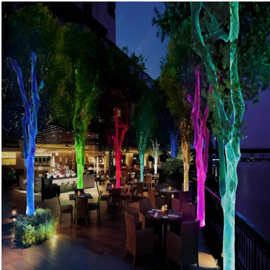 Colorful fiber optic woven mesh decorating trees in an outdoor dining area at night, creating a vibrant ambient lighting effect.