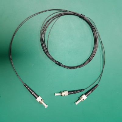 ST-1 1x2 optical splitter connector close-up, showing black fiber optic cables with metal threaded connectors and transparent ferrules on a green background